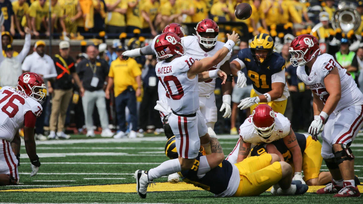 Oklahoma quarterback throws a pass as players collide during a football game