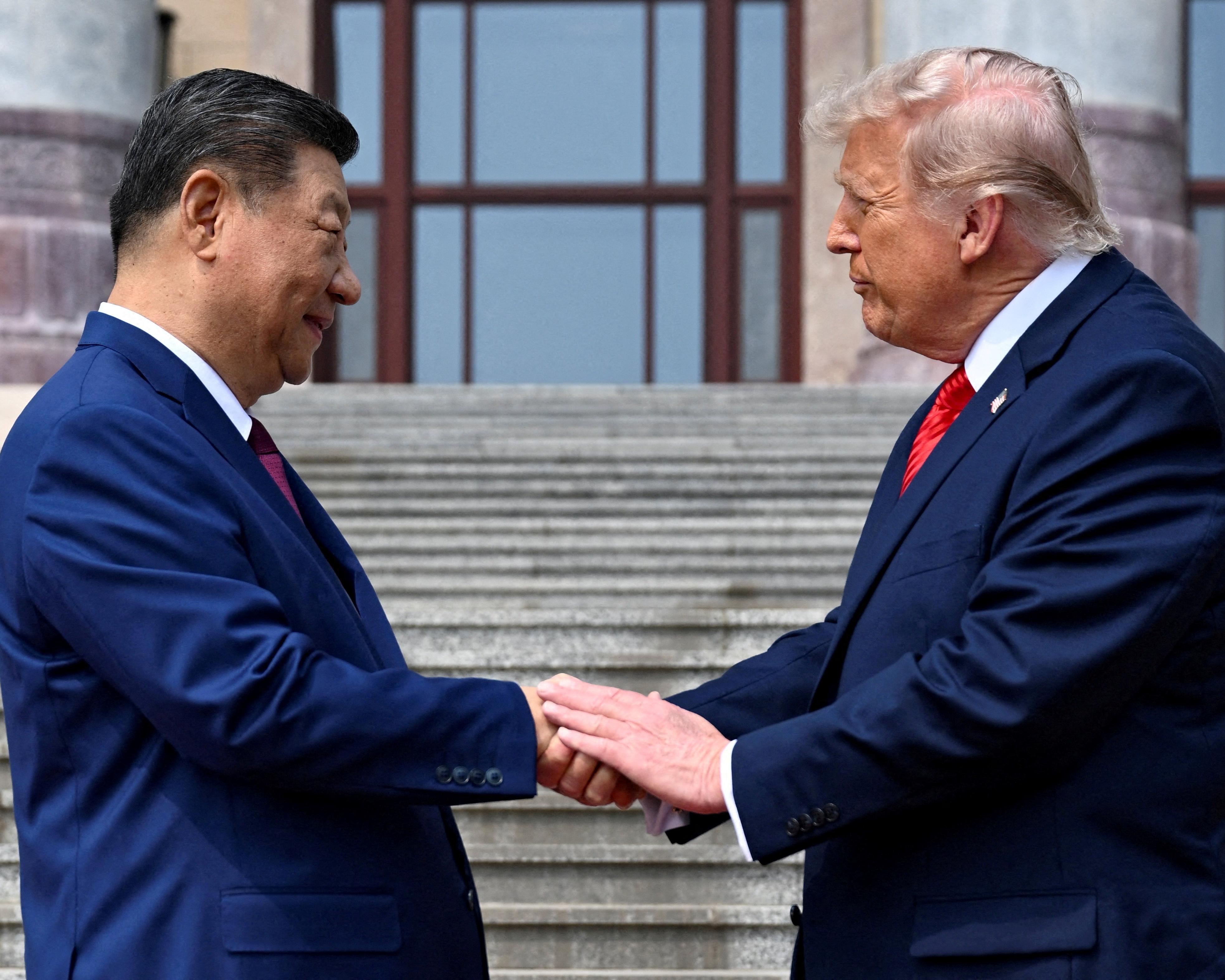 Two suited men shake hands on outdoor steps in front of a large window.