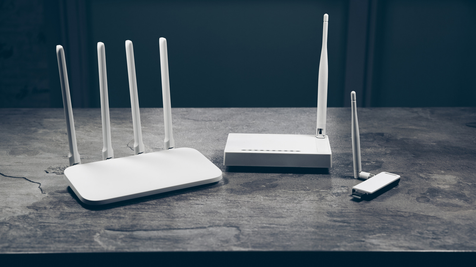 White wireless routers with upright antennas and a USB network adapter sit on a gray stone surface.