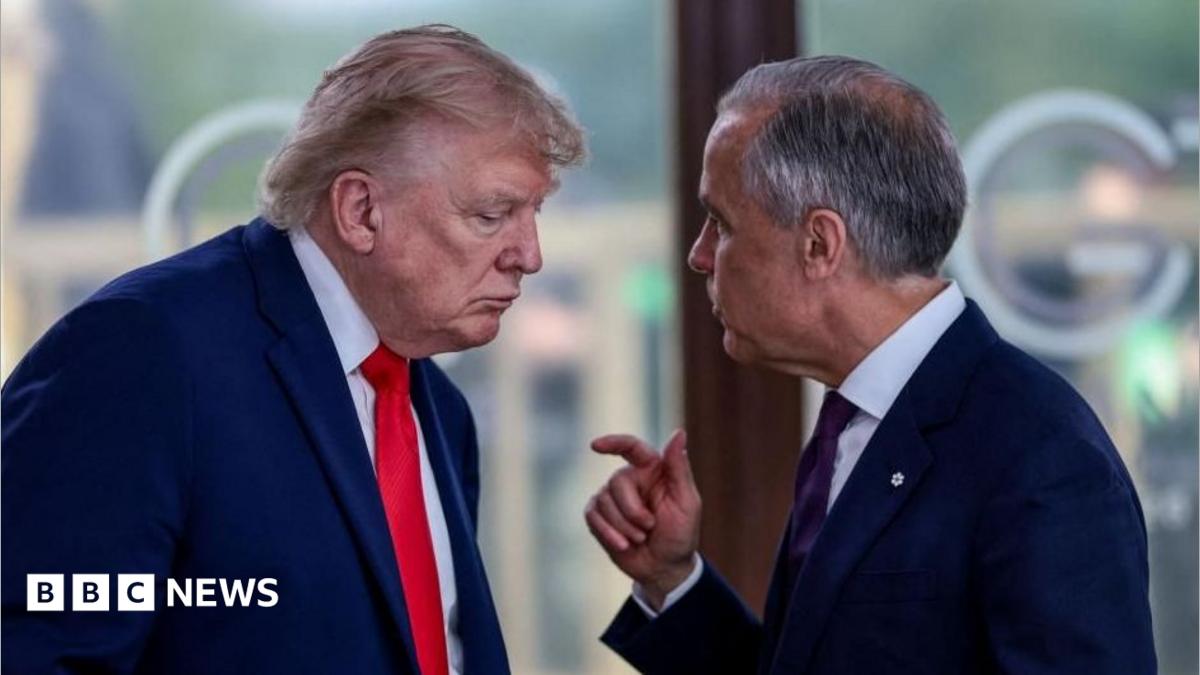 Two suited men converse closely, one gesturing with his hand, in an indoor setting.