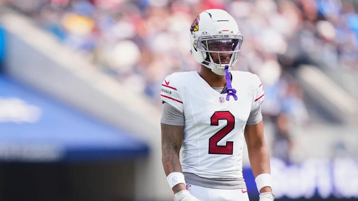 Football player wearing a white Cardinals uniform and helmet stands on the field.