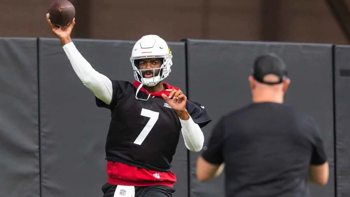 Football player wearing helmet and number 7 jersey raises a football during practice.