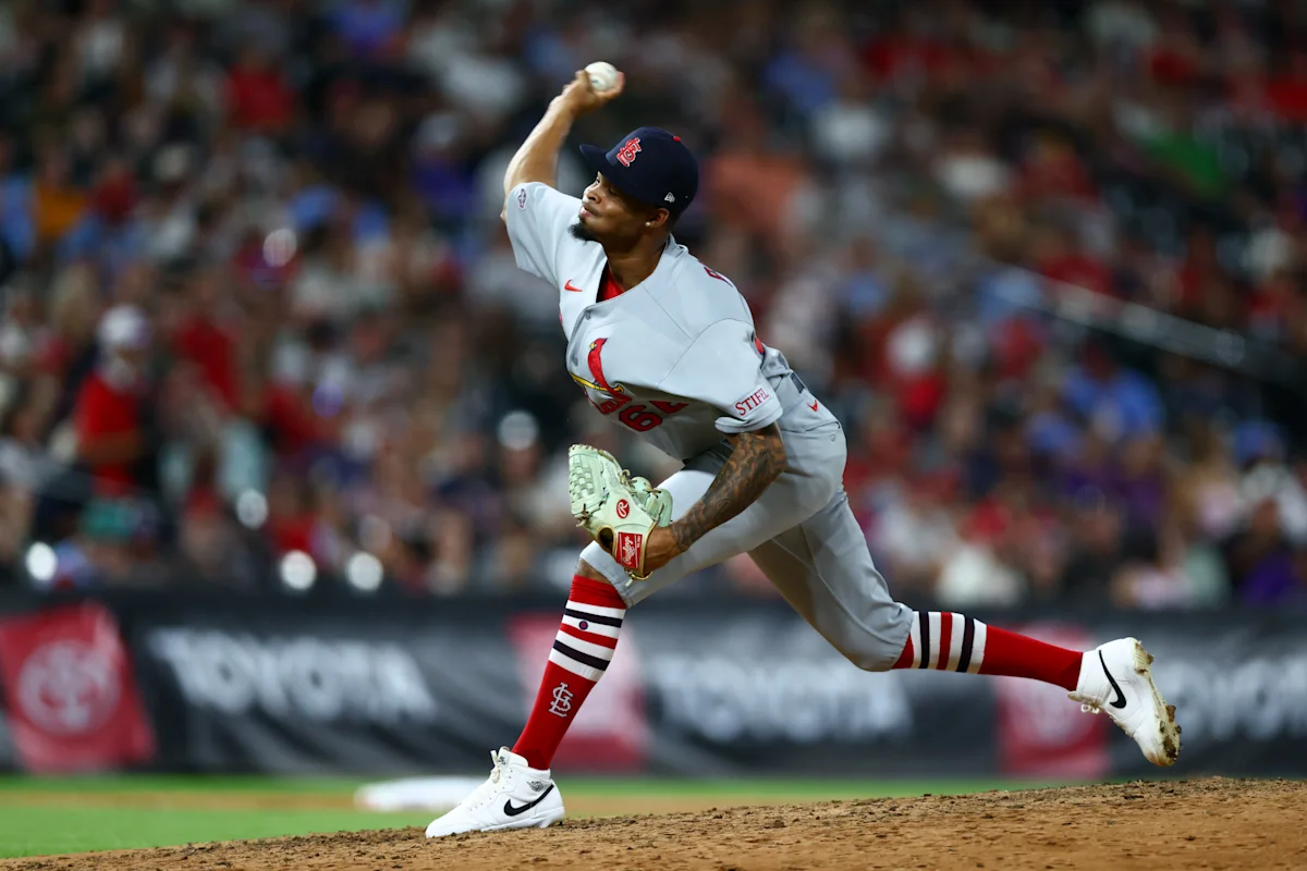 Cardinals pitcher in uniform throws a baseball during a game as a blurred crowd watches