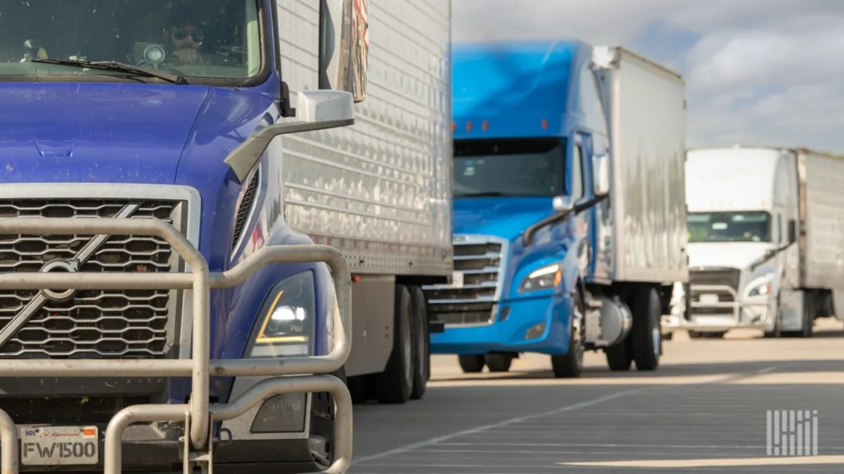 Line of blue and white semi-trucks parked in an industrial loading area.