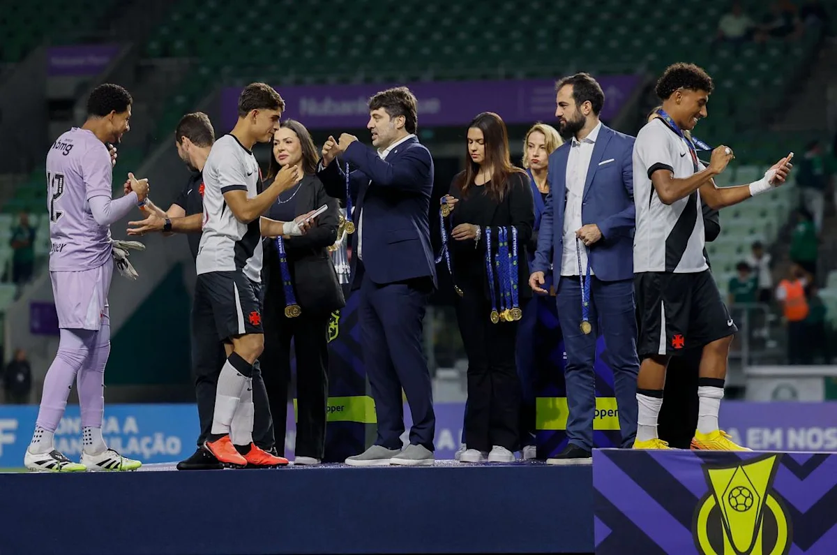 Football players and officials stand on a podium during a medal and trophy presentation.