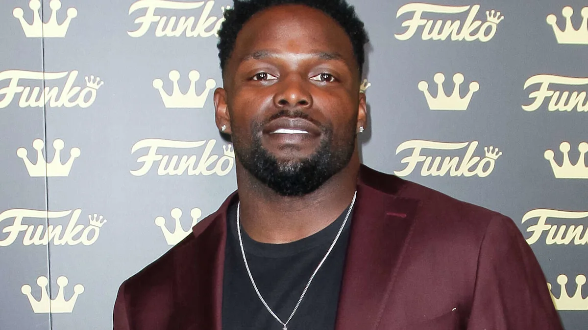 Man with short hair and a beard wearing a burgundy jacket against a branded backdrop.