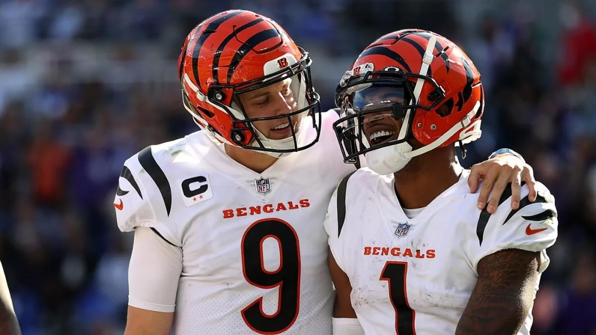 Two Cincinnati Bengals players in helmets and white uniforms smiling together on the football field
