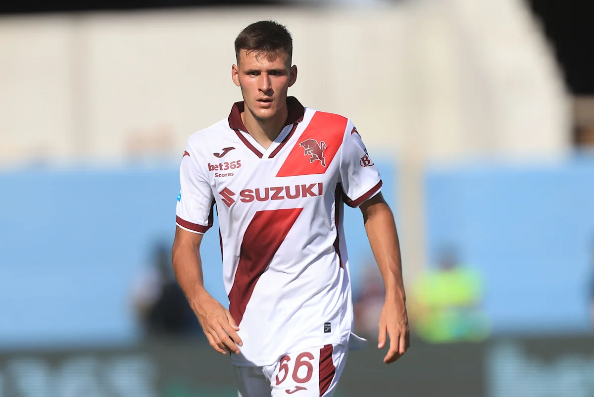 Footballer wearing a white-and-red jersey walks across the pitch during a match.