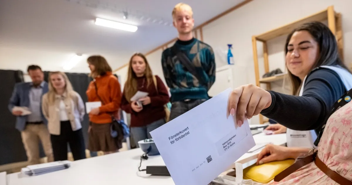 Woman holds a Swedish election ballot envelope beside voters gathered around a table indoors