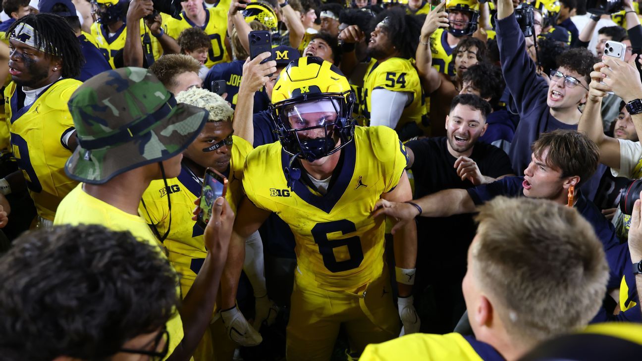 Michigan football player in yellow uniform celebrates amid cheering fans and teammates after a game