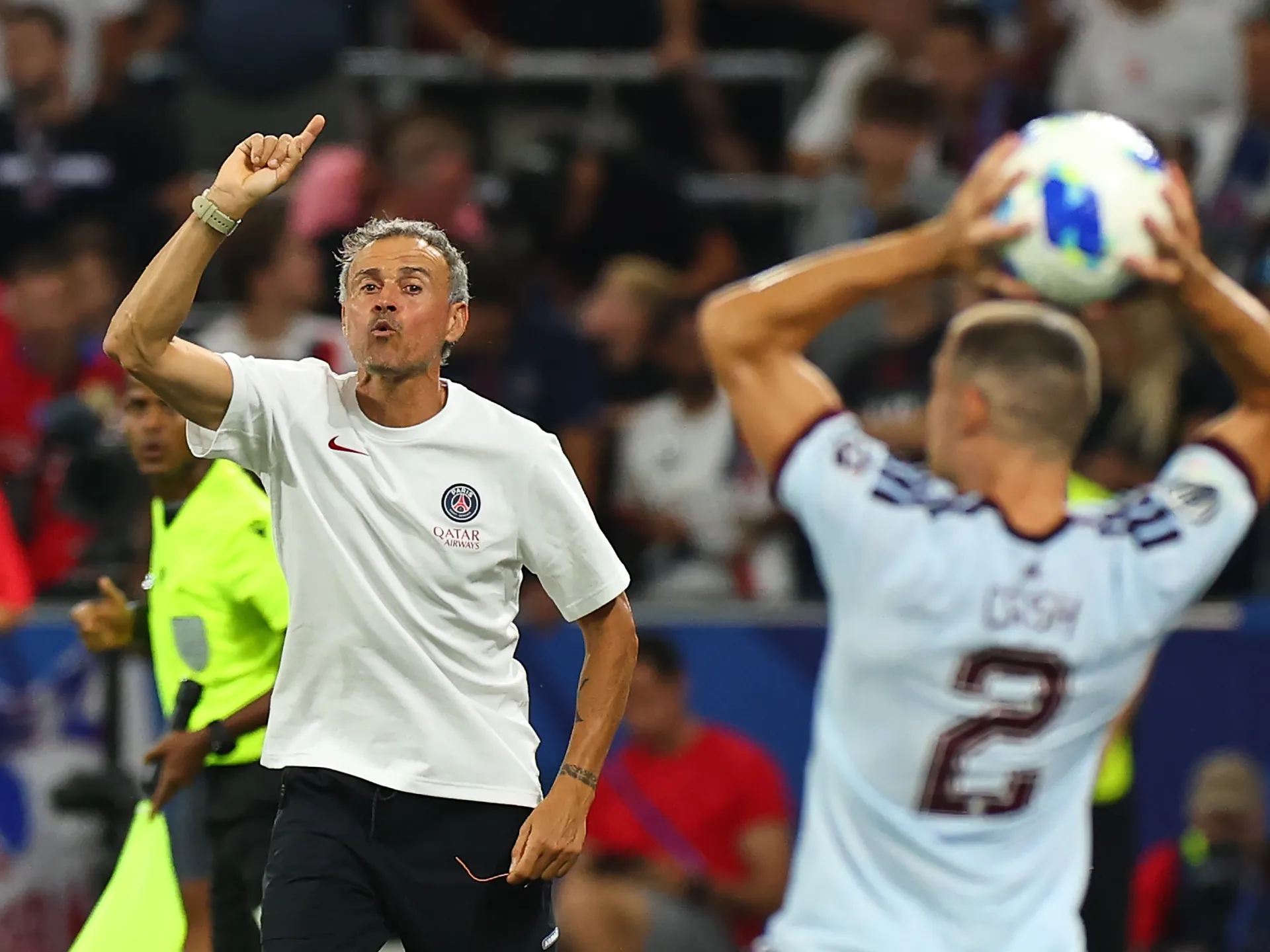 Football coach gestures while opposing player prepares to throw the ball during a match