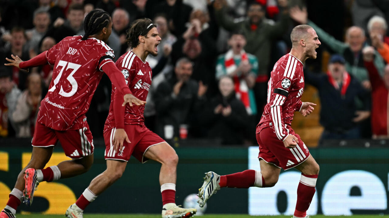 Liverpool players in red kits run and celebrate in front of cheering supporters.