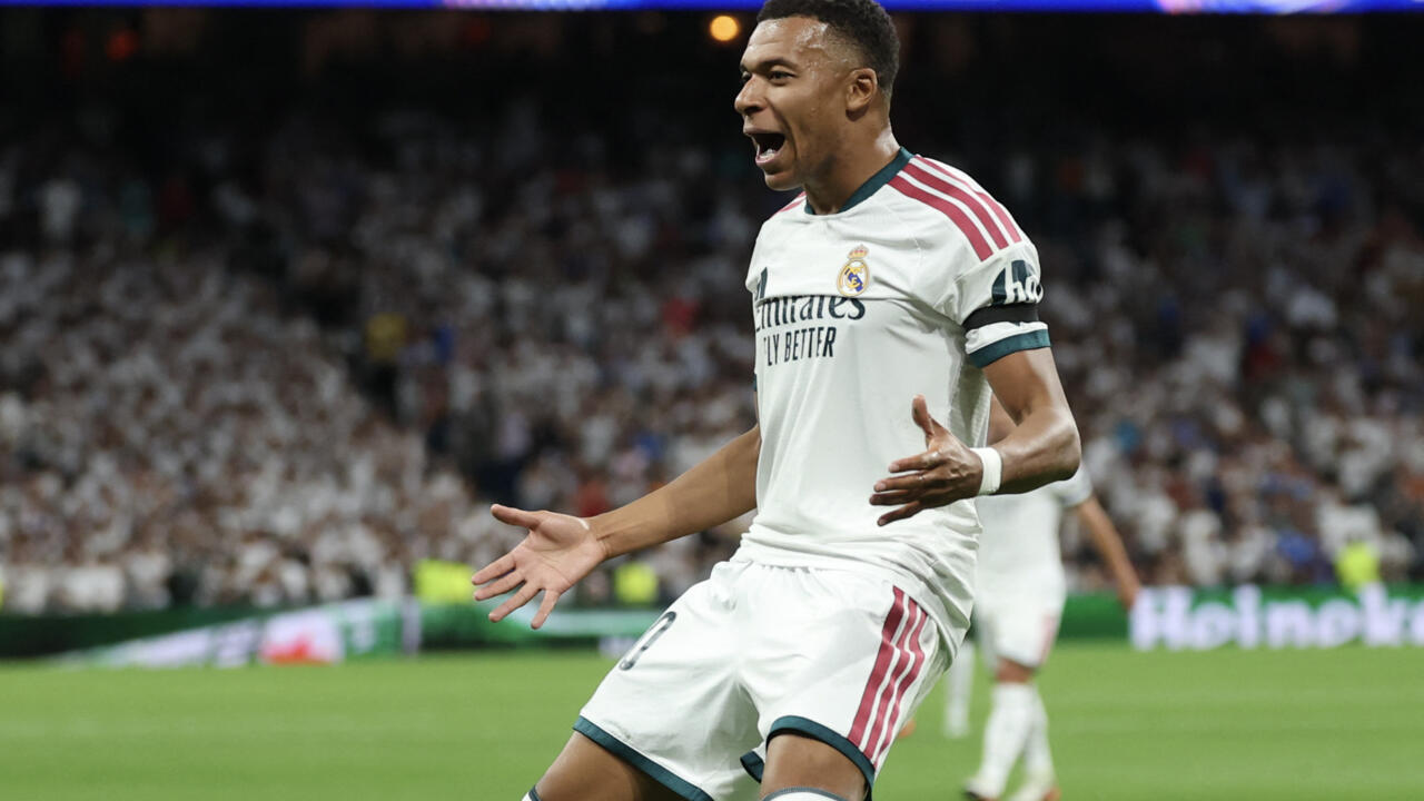 Real Madrid forward Kylian Mbappé celebrates during a match, arms outstretched before a blurred crowd.
