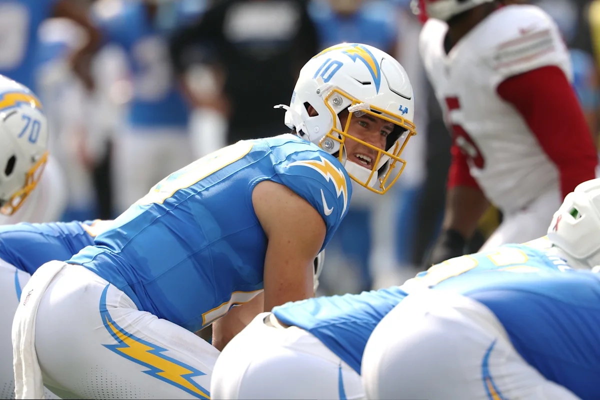 Chargers quarterback crouches behind teammates before a play, with opposing players visible in the background.