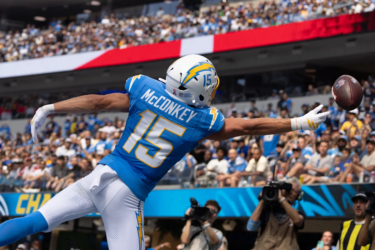 Chargers player in blue jersey dives toward a football as photographers capture the play