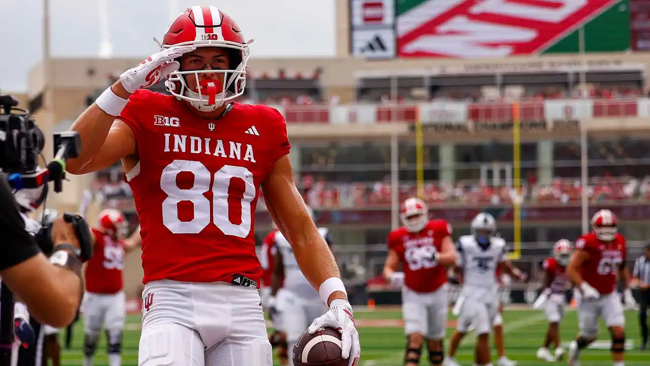 Indiana football player wearing No. 80 salutes while holding a football on the field