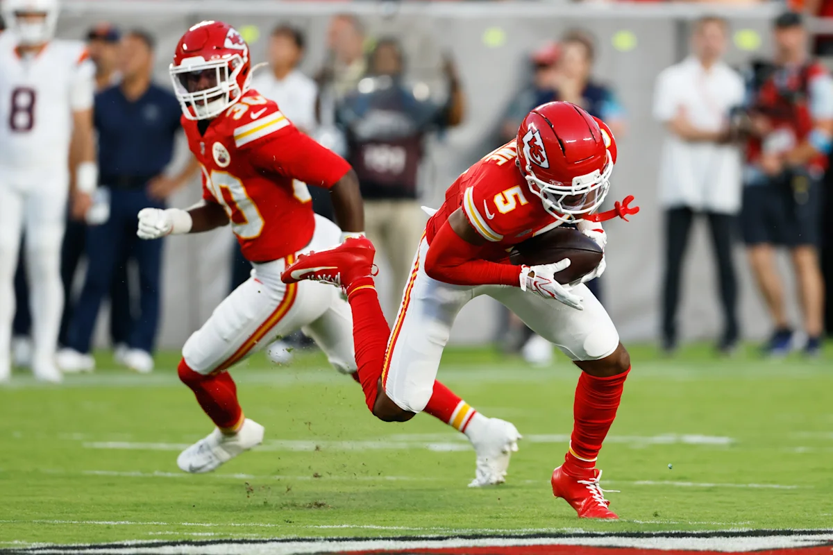 Two Kansas City Chiefs players in red uniforms run across the field during a football game.