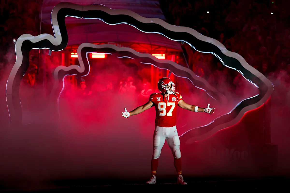 Football player in red uniform stands amid red smoke beneath illuminated team-shaped entrance structure