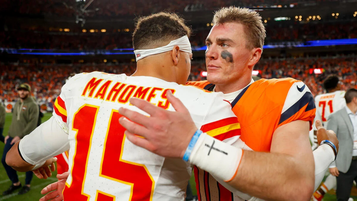 Two football players embrace on the field, with one wearing a Chiefs jersey and the other a Broncos uniform.