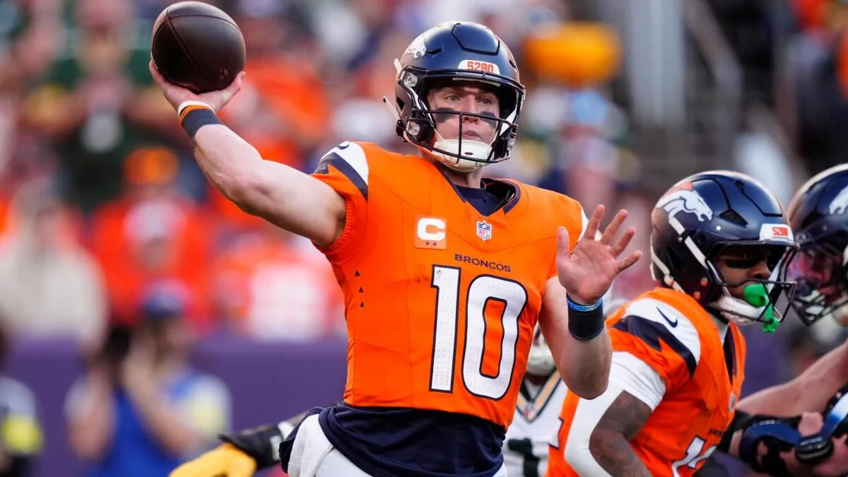 Denver Broncos quarterback throws a football during an NFL game as teammates block nearby.