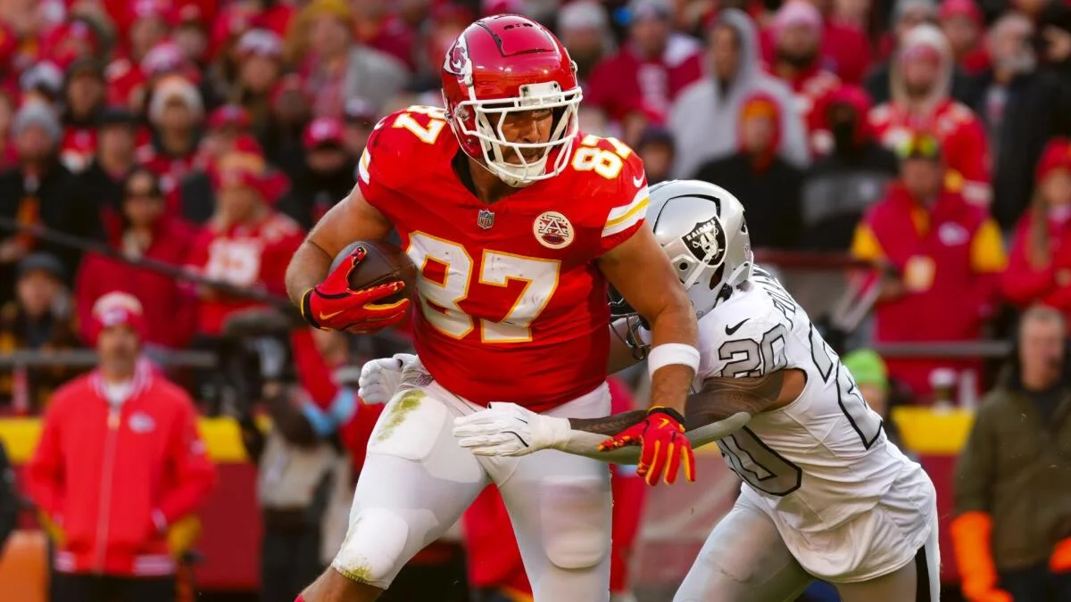 Kansas City player runs with football as a Raiders defender attempts a tackle.