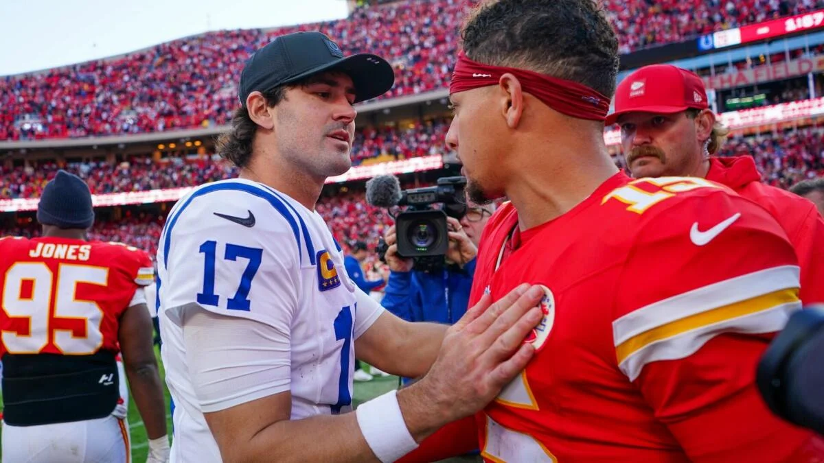 Two NFL quarterbacks in opposing uniforms greet each other on the field during a game.