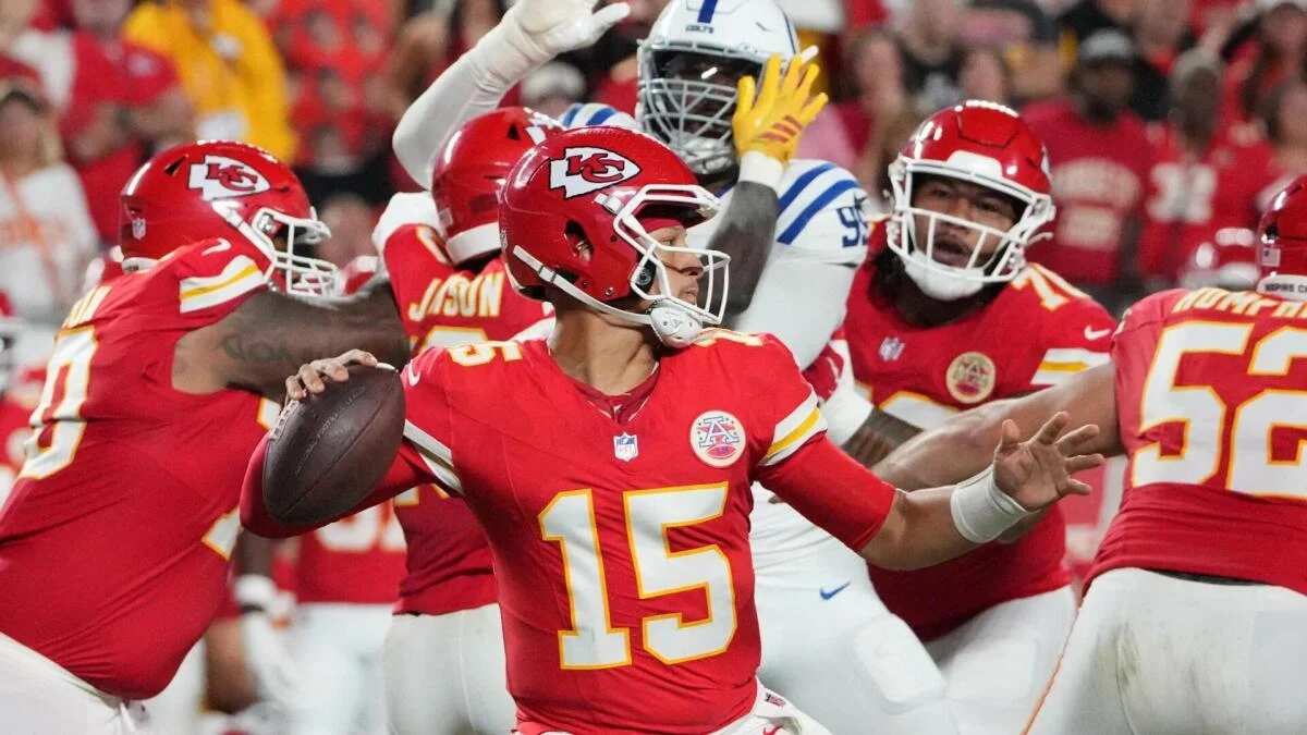 Kansas City quarterback Patrick Mahomes holds the football as players in red and white uniforms crowd around him.