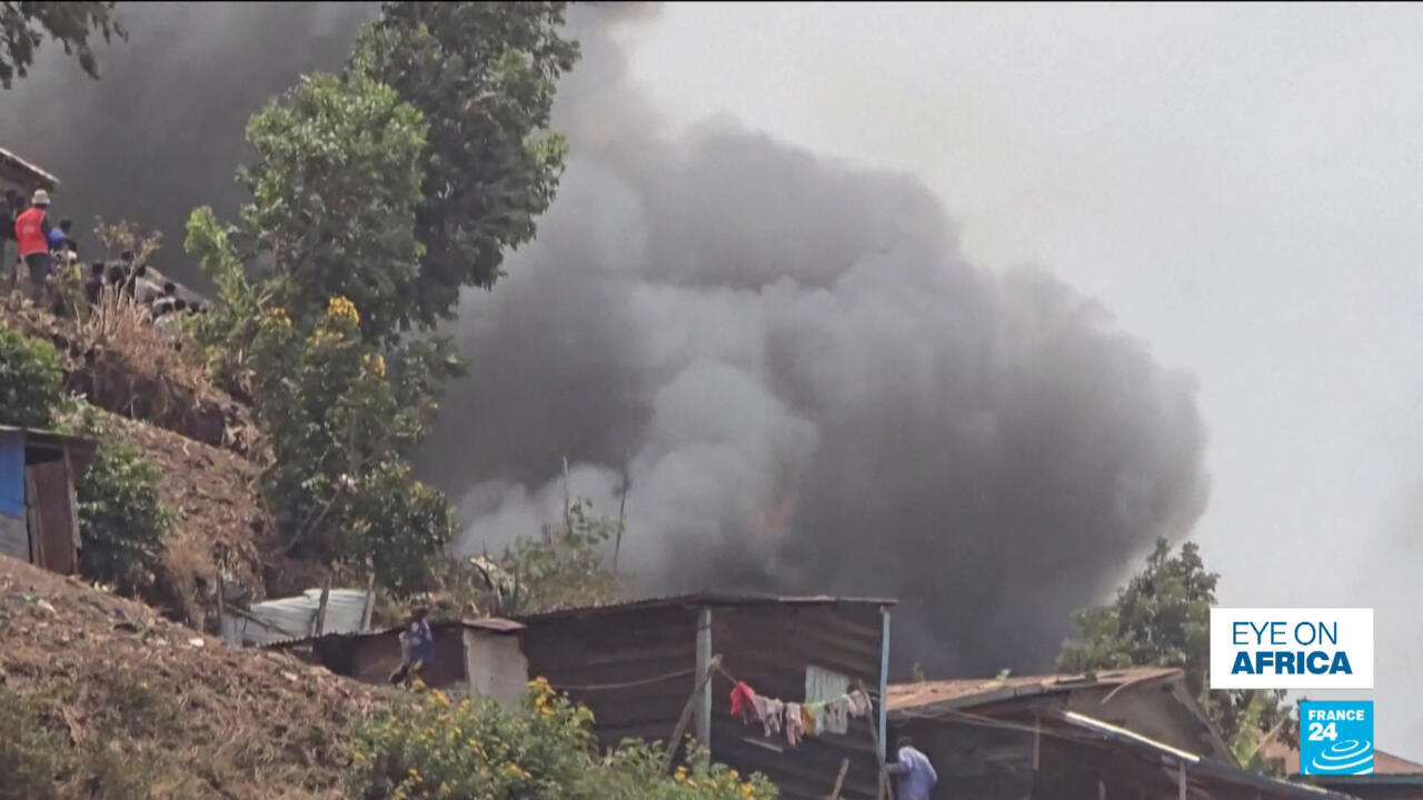 Heavy smoke billows behind hillside homes as people gather on the slope