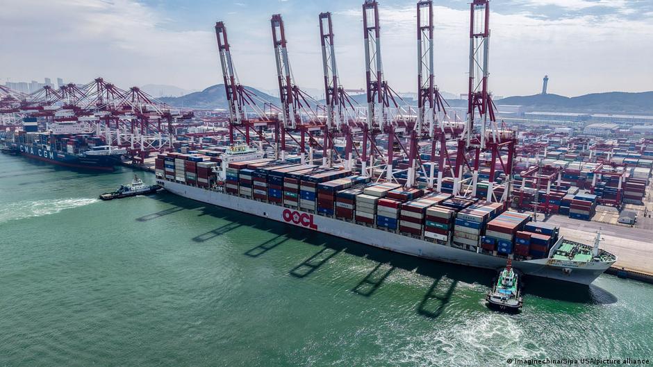 Container ship loaded with cargo containers docked beside towering cranes at a busy port.
