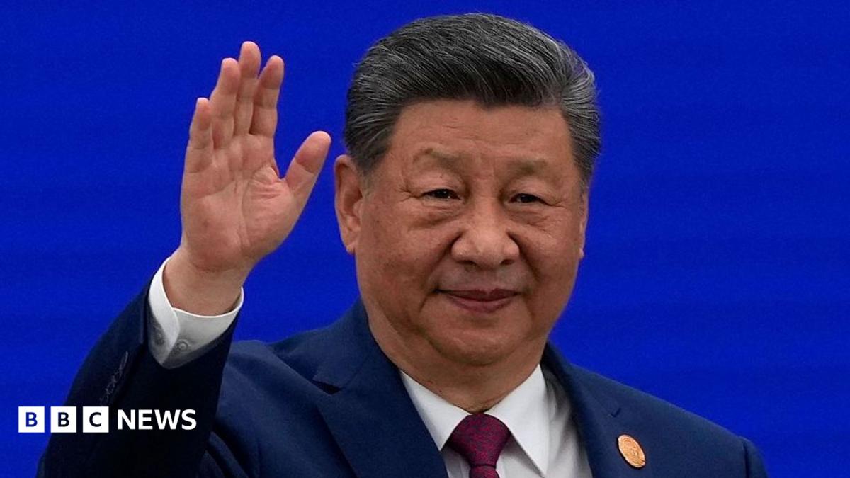 A Chinese leader in a dark suit raises his hand against a blue backdrop.