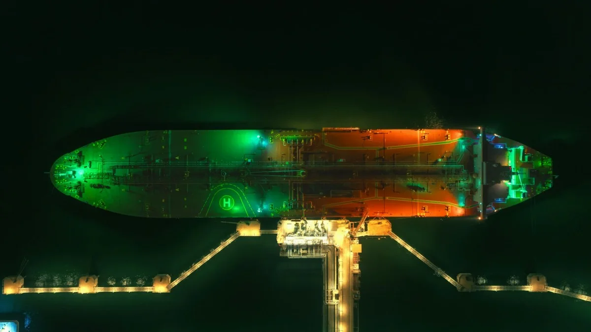 Overhead view of a large vessel docked at a brightly lit industrial pier at night.