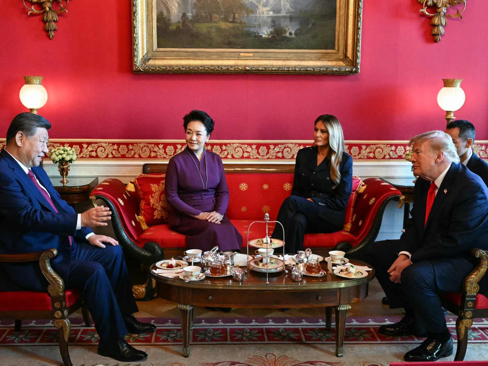 Four officials sit around a tea table in a richly decorated room, with aides behind them.