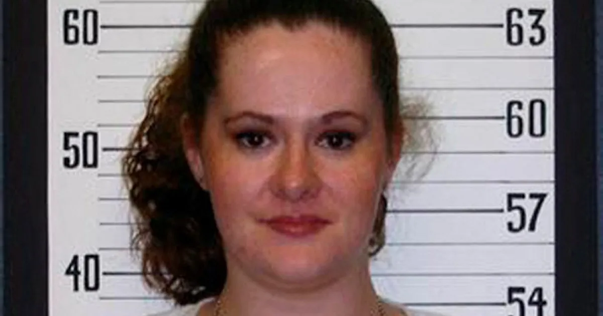 A woman with tied-back hair faces the camera in front of a numbered height chart.