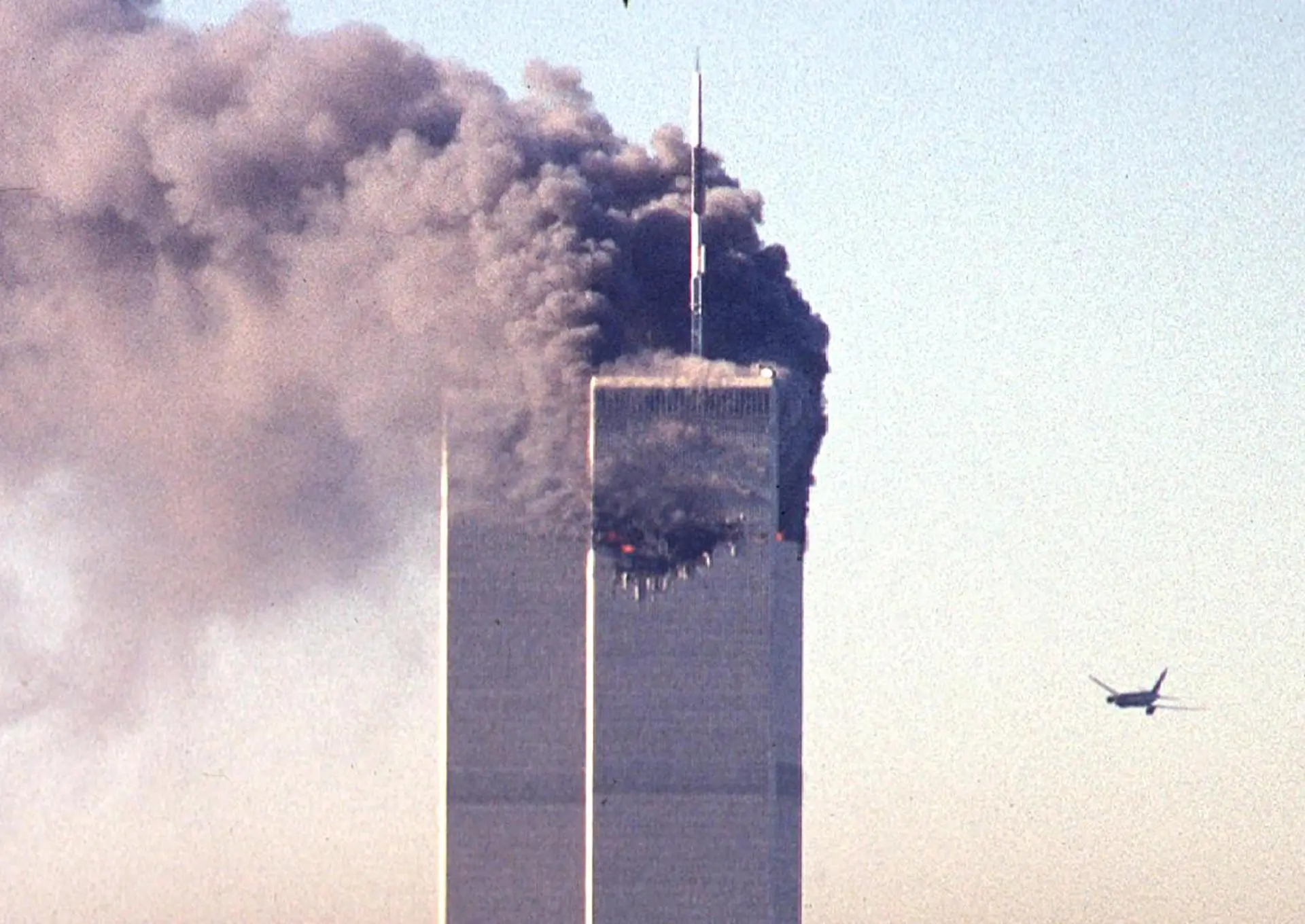 High-rise building emits heavy smoke as an aircraft flies through the nearby sky.
