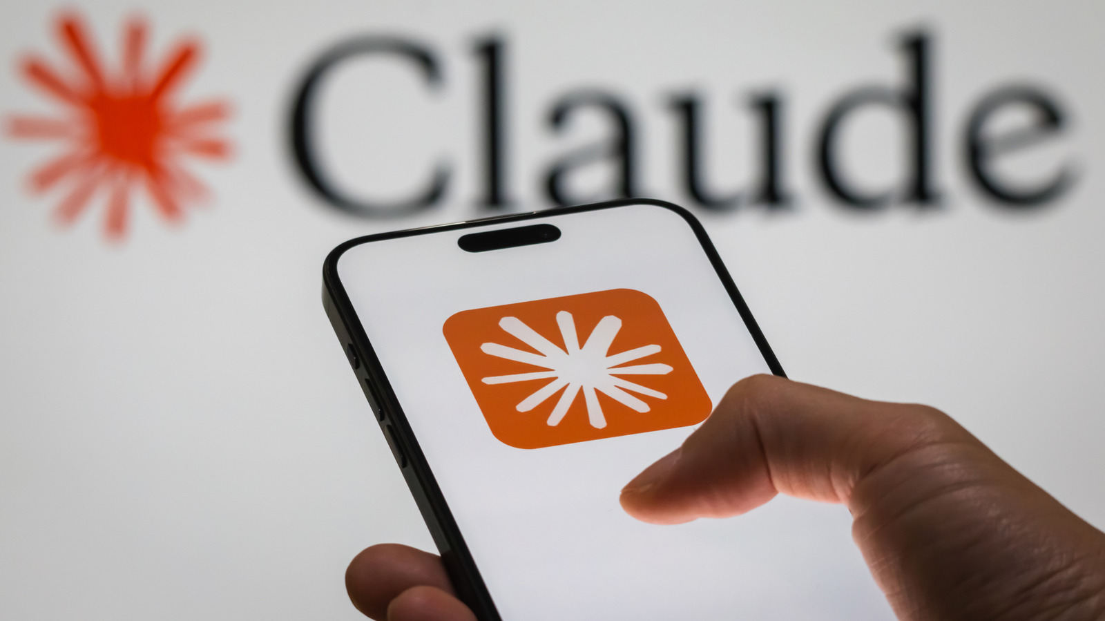 Hand holding a smartphone displaying the Claude logo against a blurred Claude wordmark