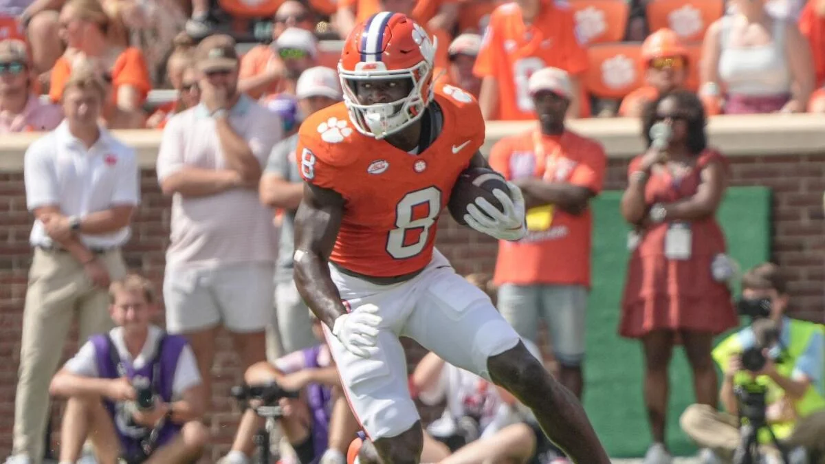Clemson player in an orange number 8 jersey runs with the football during a game.