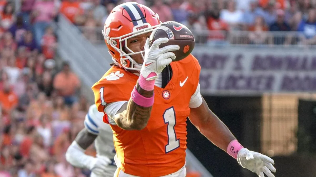 Clemson football player in orange catches a football as a teammate trails behind.