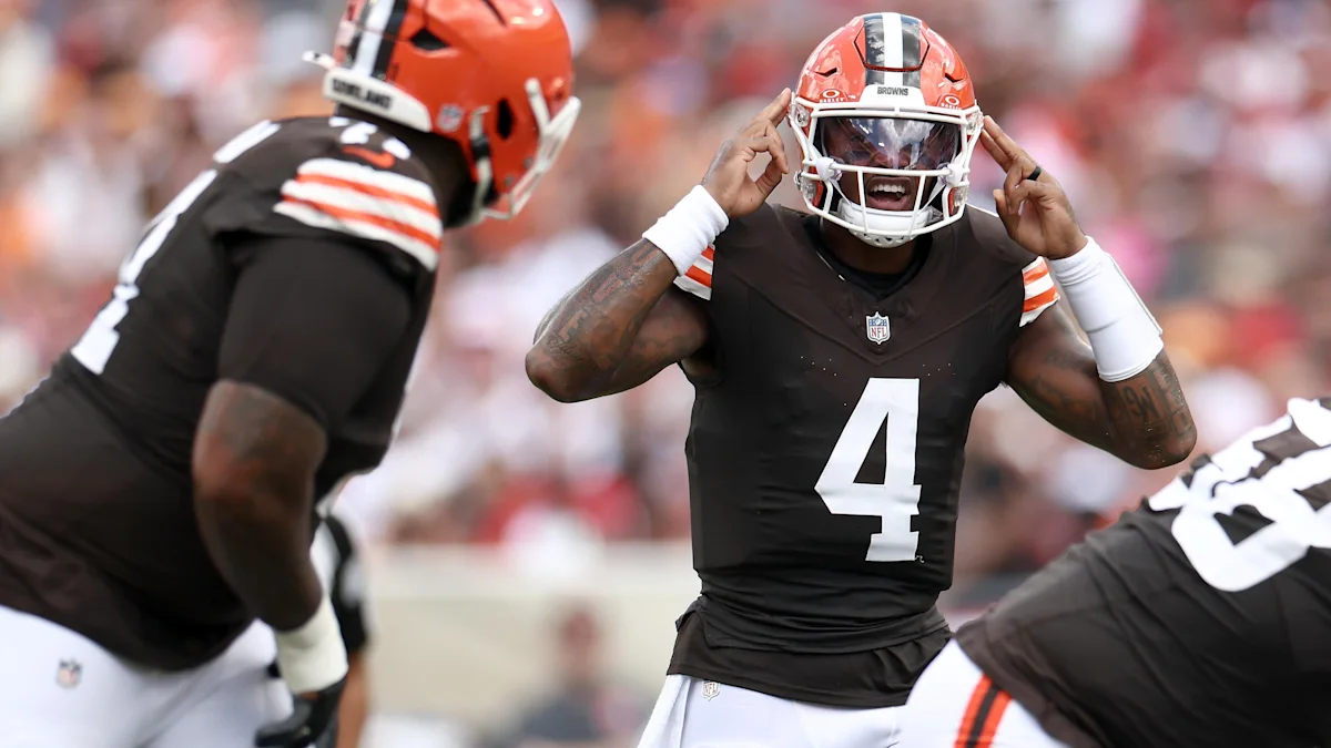 Cleveland Browns players gather on the field, with number 4 adjusting his helmet between teammates.