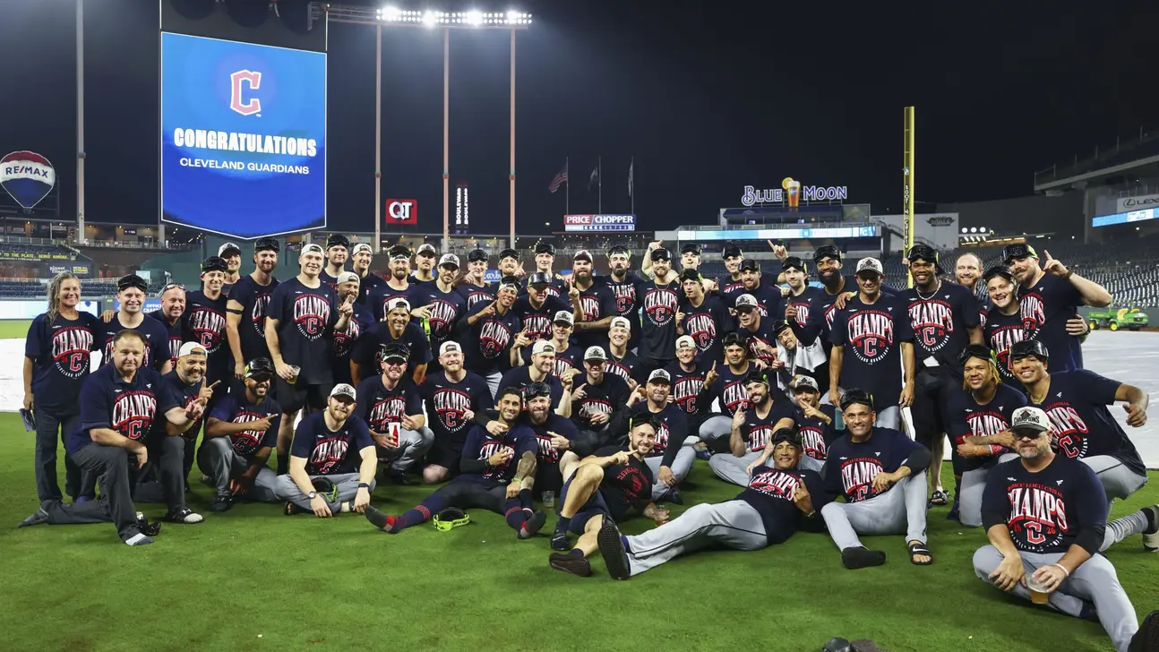 Cleveland players and staff pose together on the field beneath a scoreboard congratulating the Guardians.