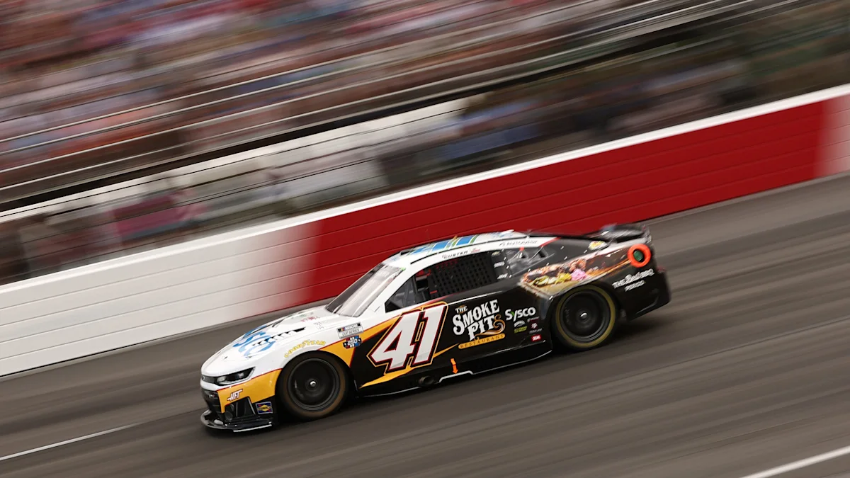 A black, white, and yellow No. 41 stock car speeds along the track beside a red wall.