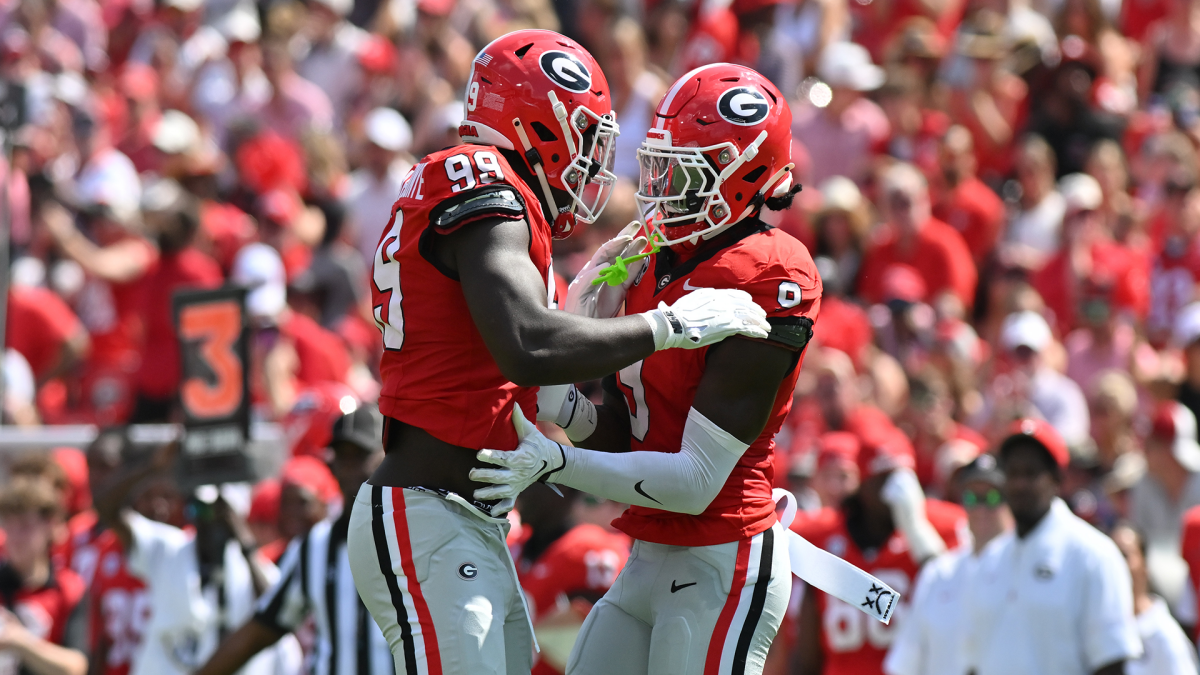 Two Georgia football players in red uniforms embrace on the field during a game.