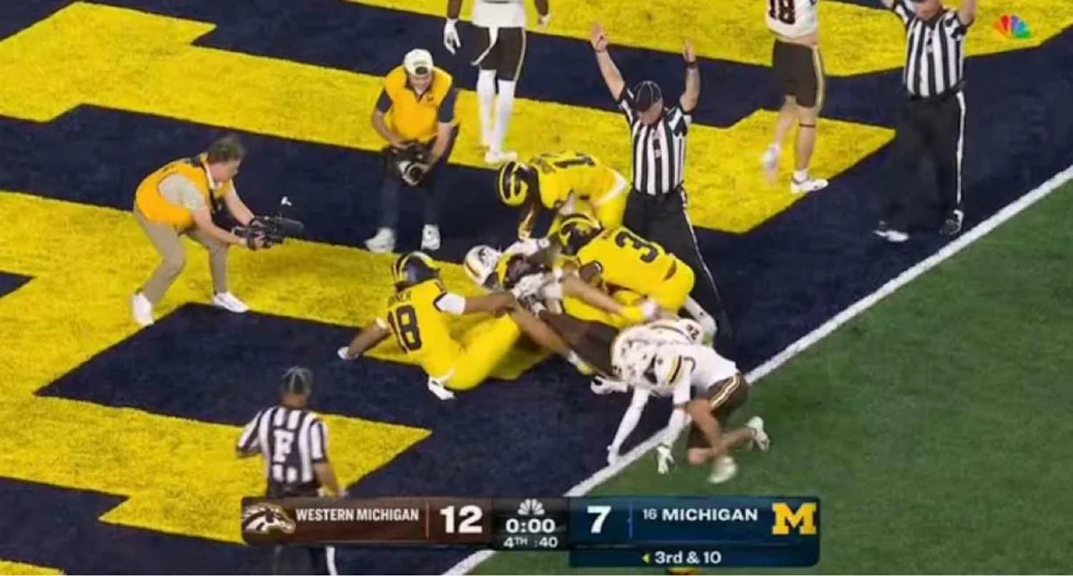 Football players pile up in the end zone as officials signal a touchdown during a college game.