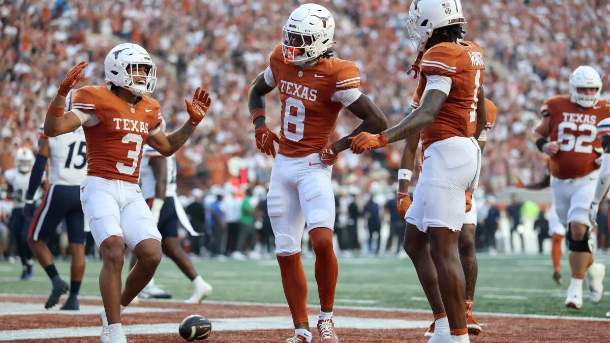 Three Texas football players in orange uniforms celebrate during a game near the end zone.