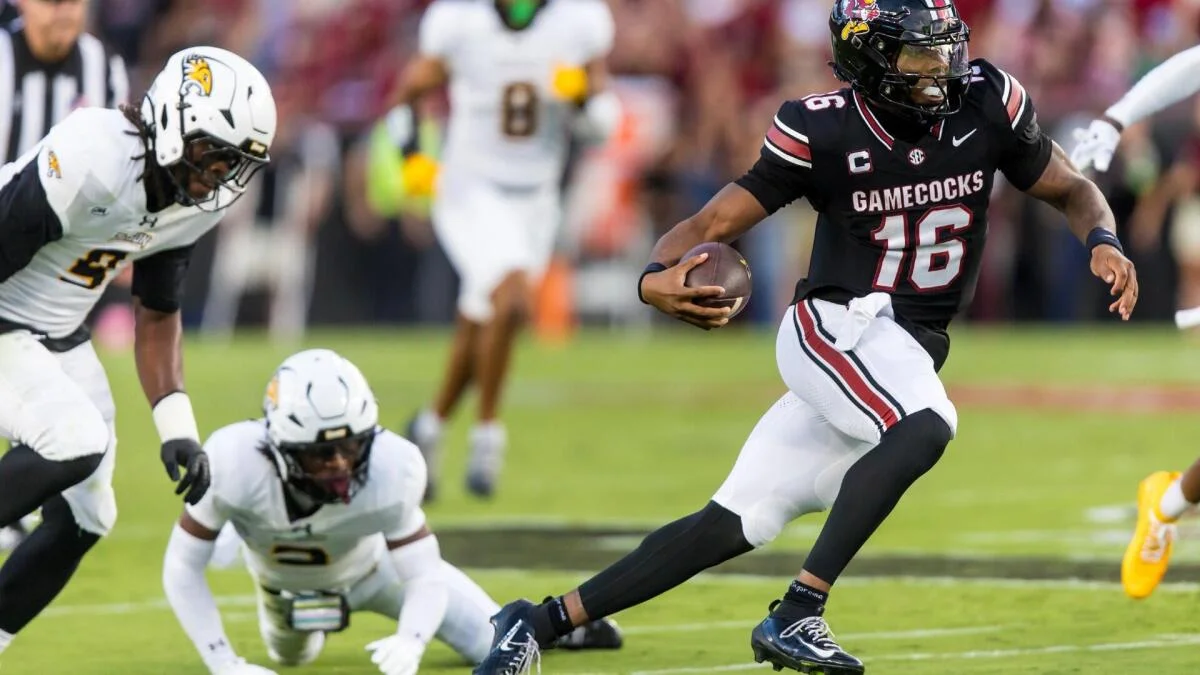 South Carolina quarterback runs with the ball as two defenders pursue during a college football game.