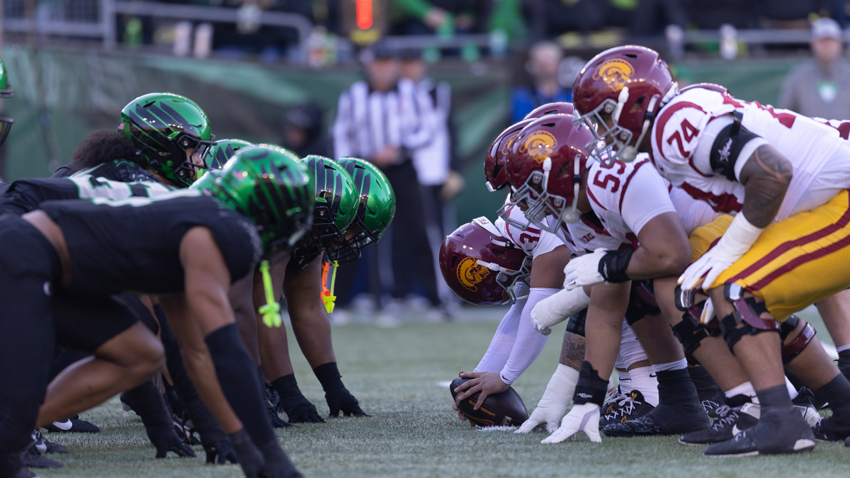 Football players in green and maroon uniforms crouch facing each other before the snap.