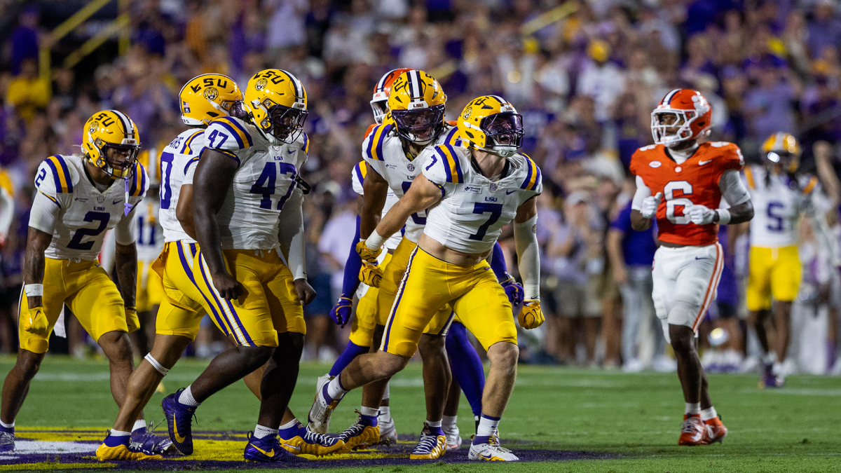 LSU football players in white and gold uniforms walk on field during a game against Clemson