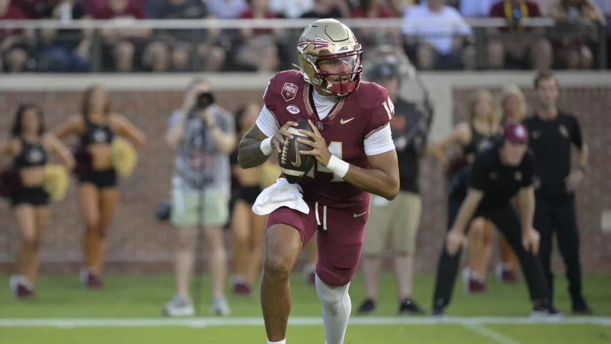 Football player in garnet uniform runs forward while holding a football during a game