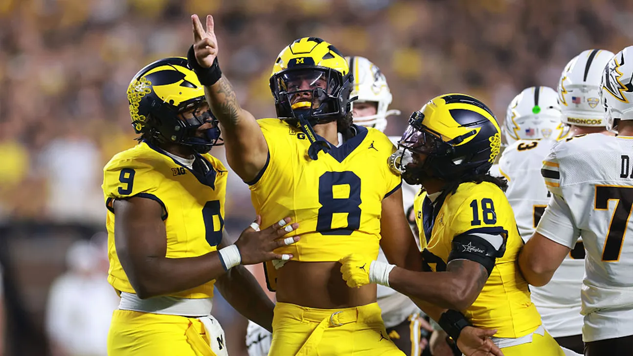 Michigan football players celebrate during a game against opponents in white uniforms.