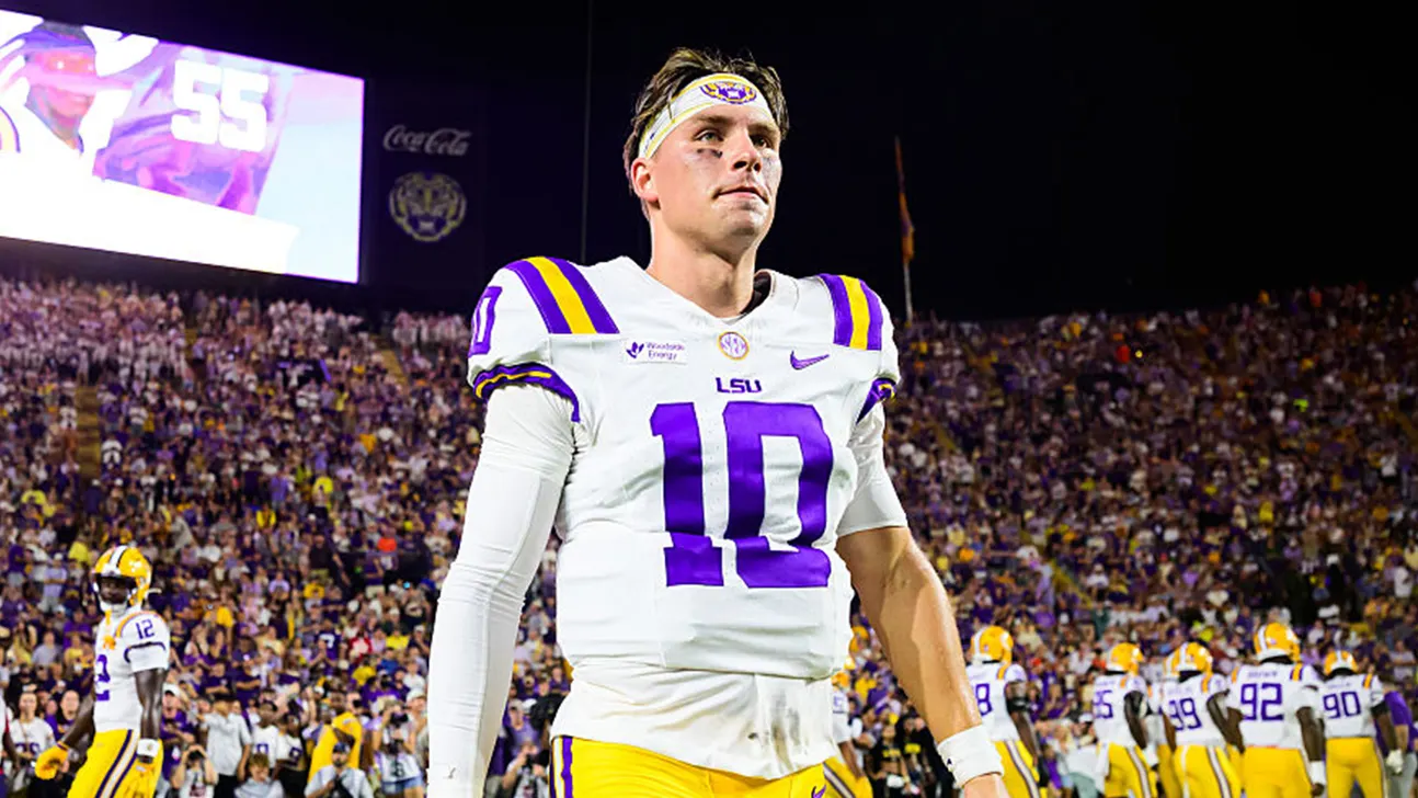 LSU football player wearing number 12 stands on the field before a crowded stadium.