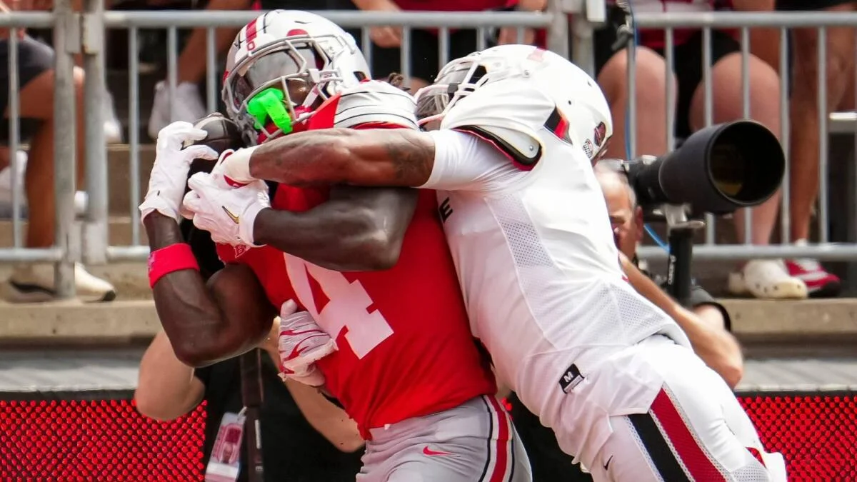 Two football players in white and red uniforms collide during a college football game.